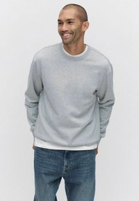 Harmaa pyöreäkauluksinen huppari kevyestä puuvillasekoitteesta, jossa on ribatty kaulus ja hihansuut, yhdistettynä vaaleansinisiiin farkkuihin.