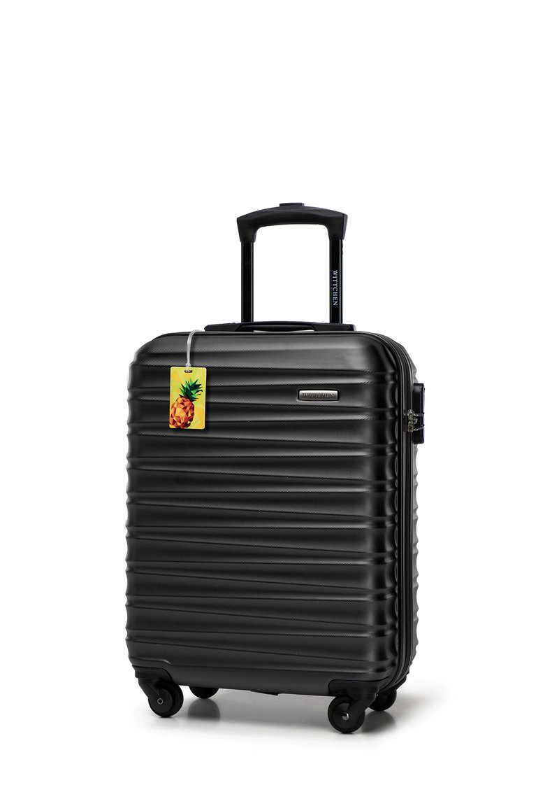Black hard-shell suitcase with a ribbed texture, retractable handle, four wheels, and a pineapple-shaped luggage tag attached.