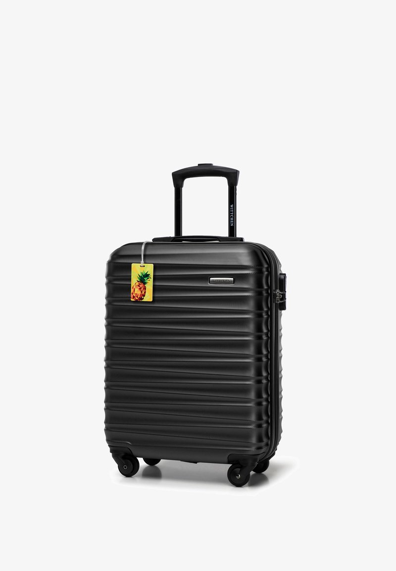 Zwarte harde koffer met een geribbelde textuur, uitschuifbare handgreep, vier wielen en een ananasvormig bagagelabel eraan bevestigd.