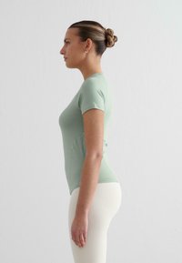 Ljusgrön kortärmad skjorta med en figurnära design, slät textur och sid sömmar; bärs med krämfärgade leggings.