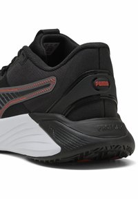 Chaussure de sport noire avec tige en mesh, accents réfléchissants et semelle intermédiaire blanche rembourrée. Présente un logo PUMA et une semelle extérieure en caoutchouc texturé.