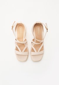 Beige stroppete kilehæle sandaler med firkantet tå, med en glat struktur, ankelrem og et diskret logo på indersålen.