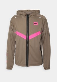 Nike gewatteerde jas in bruin, met een roze chevronontwerp, zwarte rits en paneelaccenten. Gemaakt van lichtgewicht materiaal.