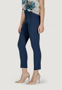Pantaloni aderenti blu navy con una texture liscia, dotati di una vita a media altezza e di una lunghezza cropped, abbinati a scarpe con tacco nude.