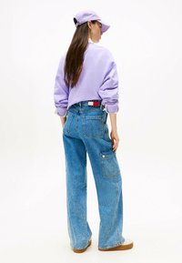 Sudadera lila con hombros caídos, jeans de pierna ancha azul con un bolsillo lateral y sandalias de plataforma color beige. Conjunto casual.