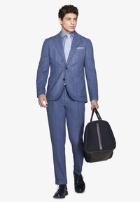 Suit blu a righe con giacca monopetto, pantaloni coordinati e cravatta a motivi blu chiaro. Il modello tiene una borsa scura.