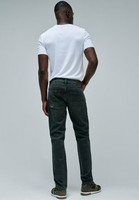 Jeans grigio scuro a taglio slim, con un design della tasca posteriore, una trama sottile e un'etichetta in pelle marrone in vita. Indossati con una maglietta bianca.