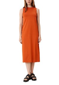 Pomarańczowa sukienka z bawełny bez rękawów o prostym kroju, długości do kolan, w zestawieniu z czarnymi, masywnymi sandałami. Brak widocznych wzorów lub detali.