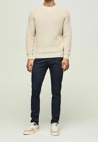Beige stickad tröja med rund neckline, parat med navy slim-fit byxor och vita sneakers med beige detaljer. Texturerat material.