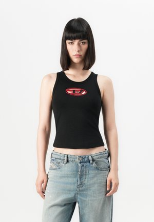 Top corto nero con un logo rosso e bianco rotondo al centro; abbinato a jeans larghi blu chiaro. Tessuto liscio, design aderente.