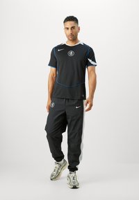 Black athletic outfit featuring a short-sleeve shirt with blue accents and logo, paired with black pants and gray side stripes.