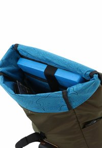 Zaino roll-top con tessuto esterno verde oliva e interno blu caratterizzato da un motivo topografico. Contiene un oggetto in legno blu fissato all'interno.