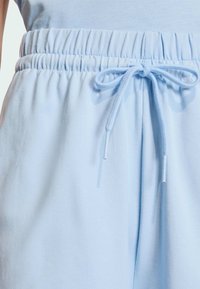 Svijetloplave trenirke s elastičnim pojasom i vezicom. Mekani pamučni materijal s glatkom teksturom i vidljivim detaljima šivanja.