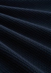 Tissu texturé bleu marine foncé présentant un motif en nid d'abeille, avec des rangées et des plis distincts, créant une apparence ondulée. Matériau doux et léger.