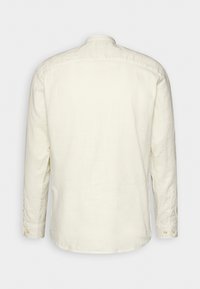 Maglietta a maniche lunghe color beige chiaro in tessuto di lino, con colletto alla coreana, polsini con bottone e taglio dritto. Texture liscia con una leggera lucentezza.