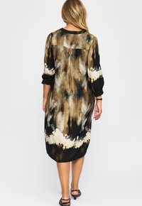 Svart och brun tie-dye midiklänning med pösiga ärmar, med rund halsringning och hög-lågt nederdel. Slen tygtextur.
