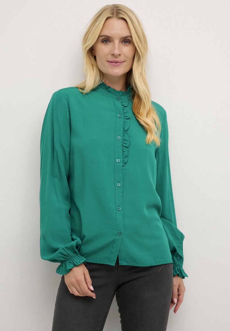 Blusa blu verde con colletto a volant e patta dei bottoni, maniche lunghe a palloncino con polsini arricciati, tessuto morbido e vestibilità comoda.