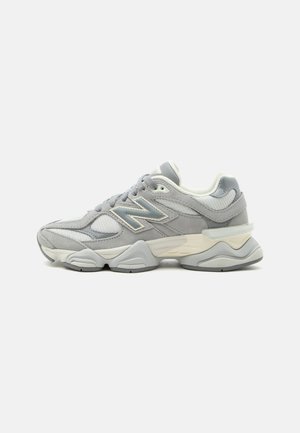 Baskets New Balance grises et blanches avec tige en mesh et suède, semelle épaisse avec motifs ondulés et fermeture à lacets, vues de profil.