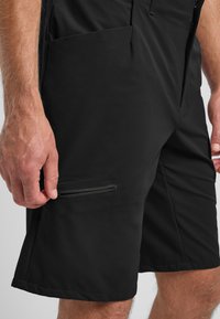Schwarze Shorts aus leichtem Stoff mit glatter Textur. Zu den Merkmalen gehören Seitentaschen und eine kleine Reißverschlusstasche am Oberschenkel.