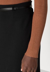 Stickad brun ribbad långärmad topp i kombination med en figurnära svart kjol, accentuerad med ett tunt svart bälte i midjan.