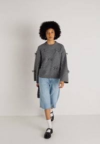 Pilka megzta palaidinė su kaspinų akcentais, plačiomis rankovėmis, derinama su šviesiais džinsiniais kelnių šortais, baltomis kojinėmis ir juodomis platforminėmis bateliais.