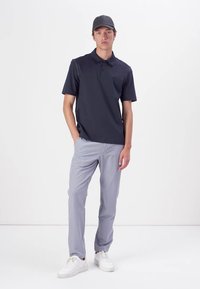 Tumed polo särk lühikeste varrukatega, nööbipaneeliga, koos heledate hallide kitsaste pükste ja valgete tossudega, kantud musta mütsiga.