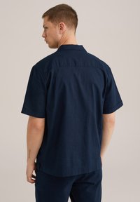 Camisa de manga corta azul marino hecha de un tejido ligero, con cuello, corte relajado y aberturas laterales para facilitar el movimiento.