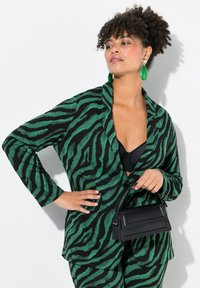 Blazer a strisce zebrate verdi e nere con maniche lunghe, tessuto testurizzato e vestibilità sagomata, abbinato a una borsa nera.