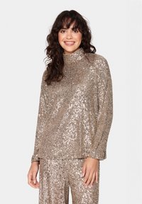 Top a maniche lunghe e colletto alto realizzato in paillettes dorate lucide, caratterizzato da una vestibilità ampia e una texture a coste, abbinato a pantaloni di paillettes coordinati.