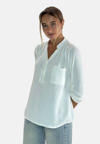 Witte blouse met lange mouwen, knoopsluiting, één borstzak en opgerolde mouwen. Soepele textuur met een iets losse pasvorm.