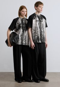 Ασπρόμαυρα, υπερμεγέθη μπλουζάκια με μοτίβα και μανίκια raglan, σε συνδυασμό με φαρδιά μαύρη παντελόνια και μαύρη τσάντα. Ομαλή υφή υφάσματος.