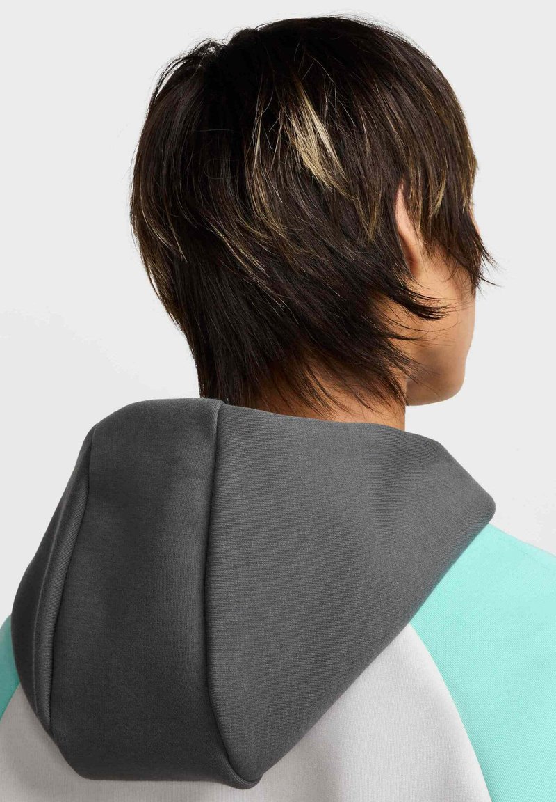 Capucha gris de una sudadera con un cuerpo verde menta y blanco. Textura de tela suave visible, con una forma relajada y redondeada alrededor del cuello.