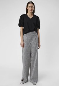 Haut noir à manches courtes avec col en V, associé à un pantalon taille haute à jambes larges rayé noir et blanc, avec une texture lisse et des chaussures argentées.