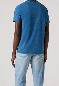 Modrá krátká košile s krátkým rukávem vyrobená z měkké bavlny, s kulatým výstřihem. V kombinaci se světle modrými vybledlými džíny. Minimalistický design, bez vzorů.