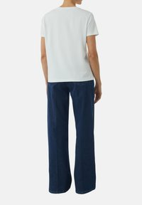 Weiße Kurzarm-T-Shirt mit Rundhalsausschnitt, kombiniert mit dunkelblauen weit geschnittenen Jeans mit Gesäßtaschen und dezenten Nähten.