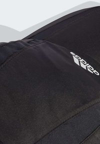 Crni atletski materijal glatke teksture, s bijelim Adidas logotipom. Dizajn uključuje zašivene panele i elegantan profil.