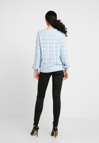 Pullover azzurro chiaro in maglia con motivo a traforato, orlo e polsini a costine. Abbinato a jeans skinny neri e scarpe nere con tacco alto.
