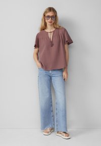 Kurzärmeliges, pflaumenfarbiges Oberteil mit Kordelzug am Hals. Kombiniert mit hellblauen, weit geschnittenen Jeans und weißen Plateausandalen. Strukturierter Stoff.