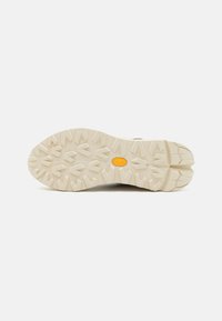 Light-colored rubber outsole with multidirectional tread pattern and a central logo. Textured surface enhances grip and traction.