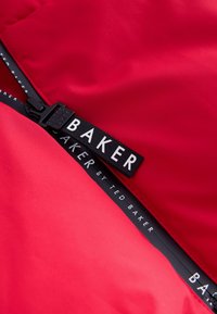 Rote Pufferjacke mit glatter Textur, Reißverschluss mit schwarzem Ziehgriff und einem schwarzen Etikett mit weißem Text.