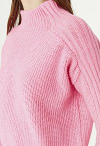 Maglione rosa lavorato a maglia con collo alto, caratterizzato da una texture a coste su spalle e maniche, che accentua calore e morbidezza.