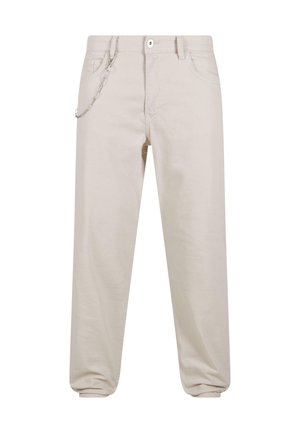 Pantalones de algodón beige con un corte relajado, que cuentan con un detalle de cadena en el bolsillo frontal y cierre de botón. Los puños se estrechan en los tobillos.