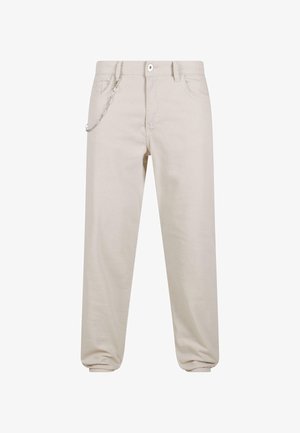 Pantalones de algodón beige con un corte relajado, que cuentan con un detalle de cadena en el bolsillo frontal y cierre de botón. Los puños se estrechan en los tobillos.