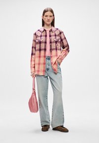 Camisa de flanela em padrão quadriculado rosa e roxo, camiseta rosa clara, jeans de perna larga azuis e uma bolsa rosa suave, combinados com sapatos de padrão de leopardo.