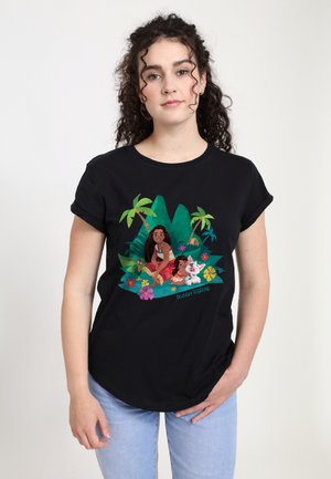 T-shirt noir avec un graphisme coloré de deux personnages dans un cadre tropical avec des fleurs et un feuillage vert.