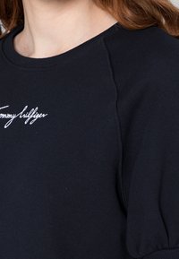 Tummansininen collegepaita, jossa on pyöreä kaula-aukko, ribatut hihansuut ja näkyvät saumat. Edessä brodeerattu "Tommy Hilfiger" -logo.