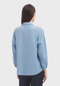 Camicia a maniche lunghe con bottoni, a righe blu chiaro, colletto, vestibilità rilassata e orlo arrotondato. Tessuto morbido e polsini leggermente affusolati.