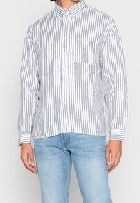 Camicia a righe in azzurro chiaro e bianco, realizzata in tessuto intrecciato, con taschino sul petto e maniche arrotolate.