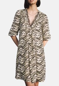 Beige kurzärmeliges Kleid mit einem schwarz-braunen Zebramuster. Verfügt über einen V-Ausschnitt mit Falten und kontrastierenden Besätzen. Weicher Stoff.