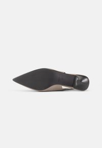 Pointed-toe shoe with a nude upper, black rubber sole, and small heel; features textured footbed and branding on the sole.